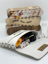 Load image into Gallery viewer, White leather wallet with sunglasses and coins, with a stack of small leather items in the background.